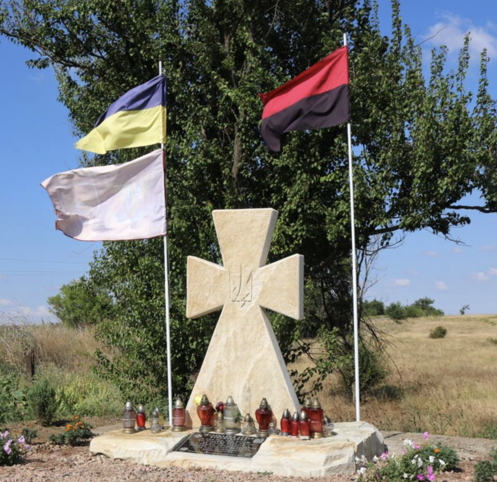козацький хрест із пісковику на могилі воїна — пам'ятник із прапорами України